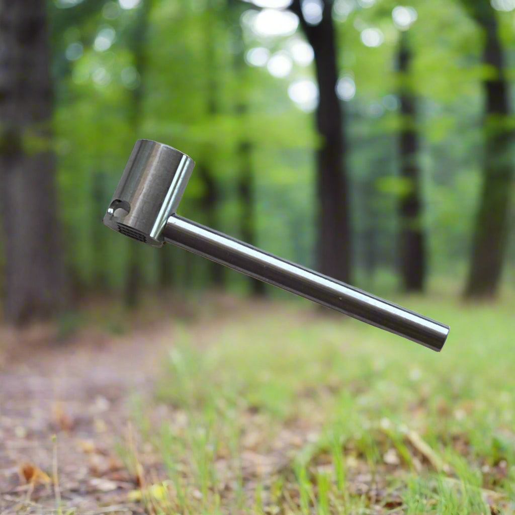 Metal tool with a cylindrical head and long handle against a forest background